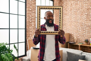 Poster - African american man putting face in empty frame angry and mad screaming frustrated and furious, shouting with anger. rage and aggressive concept.