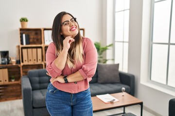 Sticker - Young hispanic woman working at the office wearing glasses smiling looking confident at the camera with crossed arms and hand on chin. thinking positive.