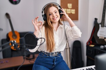 Canvas Print - Young caucasian woman recording song at music studio doing ok sign with fingers, smiling friendly gesturing excellent symbol