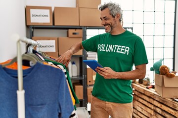 Sticker - Middle age grey-haired man volunteer using touchpad holding clothes at charity center