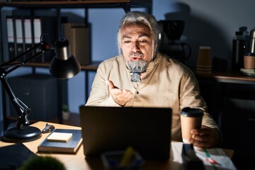 Poster - Middle age man with grey hair working at the office at night looking at the camera blowing a kiss with hand on air being lovely and sexy. love expression.