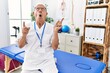 © Krakenimages.com - Senior physiotherapy man working at pain recovery clinic amazed and surprised looking up and pointing with fingers and raised arms.