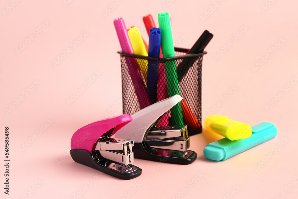 Holder with felt-tip pens and staplers on pink background