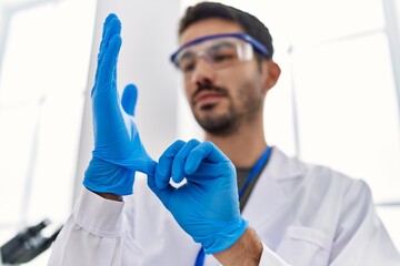 Wall Mural - Young hispanic man wearing scientist uniform and gloves at laboratory