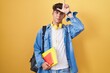Hispanic teenager wearing student backpack and holding books making fun of people with fingers on forehead doing loser gesture mocking and insulting.