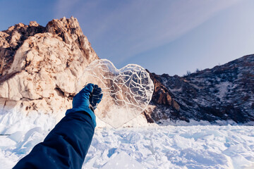 Wall Mural - Tourist hand holds crystal clear heart Arctic landscape frozen snow lake Baikal or Antarctica extreme with sun light