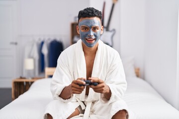 Canvas Print - Young hispanic man wearing beauty face mask playing video games smiling and laughing hard out loud because funny crazy joke.