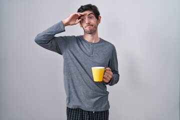 Canvas Print - Young hispanic man wearing pajama drinking a cup of coffee worried and stressed about a problem with hand on forehead, nervous and anxious for crisis