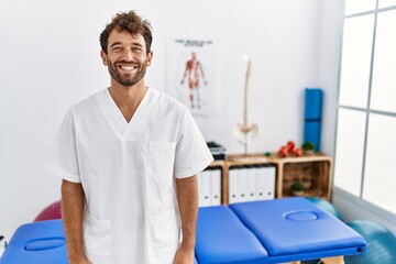 Canvas Print - Young handsome physiotherapist man working at pain recovery clinic with a happy and cool smile on face. lucky person.