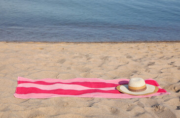 Canvas Print - Beach towel and straw hat on sand near sea, space for text