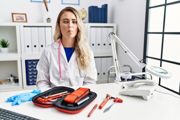 Sticker - Young beautiful doctor woman with reflex hammer and medical instruments making fish face with lips, crazy and comical gesture. funny expression.