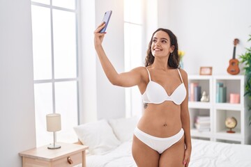 Canvas Print - Young beautiful hispanic woman make selfie by smartphone standing at bedroom