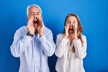 Poster - Middle age hispanic couple standing over blue background shouting angry out loud with hands over mouth