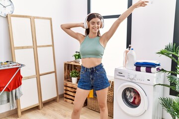 Wall Mural - Young hispanic woman listening to music waiting for washing machine at laundry room