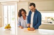 Leinwanddruck Bild - Middle age hispanic couple smiling confident cutting orange at kitchen
