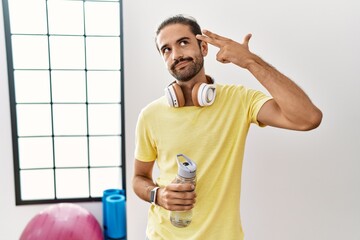 Canvas Print - Young hispanic man wearing sportswear and drinking water at the gym shooting and killing oneself pointing hand and fingers to head like gun, suicide gesture.