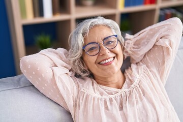 Wall Mural - Middle age grey-haired woman relaxed with hands on head sitting on sofa at home