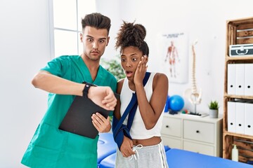 Canvas Print - Physiotherapist working with patient wearing arm on sling at rehabilitation clinic looking at the watch time worried, afraid of getting late