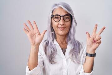 Canvas Print - Middle age woman with tattoos wearing glasses standing over white background showing and pointing up with fingers number eight while smiling confident and happy.