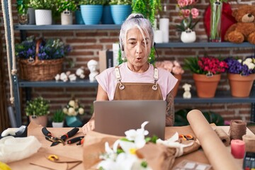 Canvas Print - Middle age woman with tattoos working at florist shop doing video call scared and amazed with open mouth for surprise, disbelief face