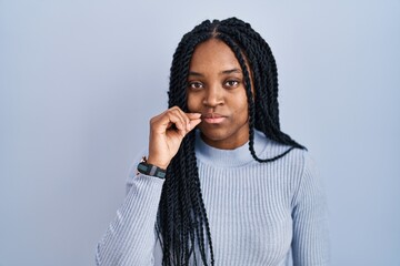 Poster - African american woman standing over blue background mouth and lips shut as zip with fingers. secret and silent, taboo talking