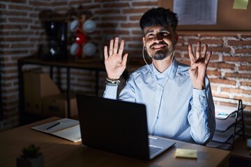 Sticker - Young hispanic man with beard working at the office at night showing and pointing up with fingers number nine while smiling confident and happy.