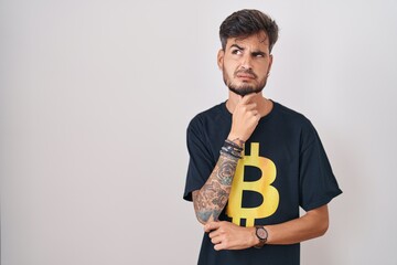 Sticker - Young hispanic man with tattoos wearing bitcoin t shirt thinking worried about a question, concerned and nervous with hand on chin