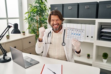 Poster - Handsome middle age doctor man holding holidays calendar screaming proud, celebrating victory and success very excited with raised arms