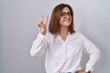 Poster - Brunette woman standing over white isolated background smiling looking to the camera showing fingers doing victory sign. number two.