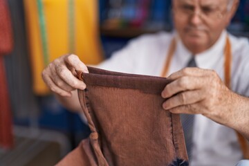 Canvas Print - Middle age grey-haired man tailor holding trousers at tailor shop