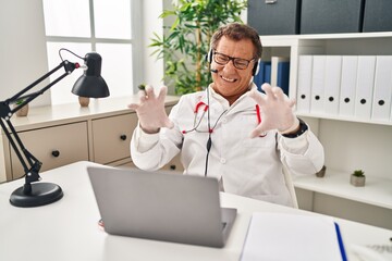 Wall Mural - Senior doctor man working on online appointment smiling funny doing claw gesture as cat, aggressive and sexy expression