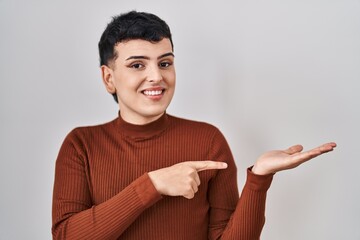 Sticker - Non binary person wearing make up standing over isolated background amazed and smiling to the camera while presenting with hand and pointing with finger.