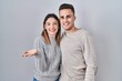 © Krakenimages.com - Young hispanic couple standing over white background smiling cheerful presenting and pointing with palm of hand looking at the camera.