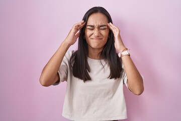 Wall Mural - Young hispanic woman standing over pink background with hand on head, headache because stress. suffering migraine.