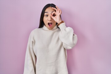 Wall Mural - Young south asian woman standing over pink background doing ok gesture shocked with surprised face, eye looking through fingers. unbelieving expression.