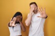 Interracial couple standing over yellow background covering eyes with hands and doing stop gesture with sad and fear expression. embarrassed and negative concept.