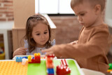 Fototapeta Pomosty - Adorable girl and boy playing with construction block pieces sitting on table at kindergarten