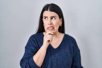 Poster - Young brunette woman standing over isolated background thinking worried about a question, concerned and nervous with hand on chin