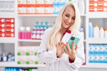 Poster - Young blonde woman pharmacist using smartphone working at pharmacy