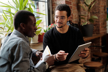 Poster - Young confident businessman with tablet communicating with male colleague during report or presentation of new project