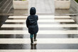 Back view of a little boy crossing the crosswalk on the road on rainy weather.