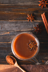 Wall Mural - Hot cocoa in cup glass with cinnamon stick, star anise and cocoa powder on wooden background, Hot drink in winter season, Table top view