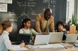 © AnnaStills - African American teacher teaching students to use computers, they discussing software sitting at table at IT lesson