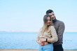 © ribalka yuli - Beautiful young couple posing on the beach against the backdrop of a large lake. Man hugging woman from behind and looking at camera