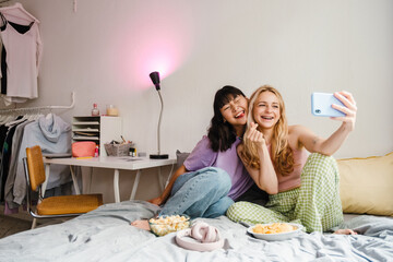 Wall Mural - Two multiracial girls making fun while taking selfie on mobile phone