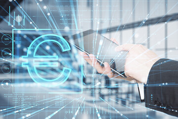 Wall Mural - Close up of businessman hand pointing at tablet with glowing euro sign hologram on blurry office interior background. Online banking, trade, finance and blockchain concept. Double exposure.