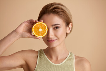 beautiful woman smiling with orange fruit. positive woman with radiant face recommended vitamin for 