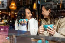 Happy Woman Talking To Friend Holding Cup In Cafe