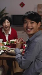 Wall Mural - Vertical Screen: slow motion of happy family at dinner table turning head and look at camera in surprise as someone is serving the main dish for reunion meal at home. text translation: fortune