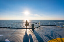UK, Scotland, Lone Woman Looking At Setting Sun From Afterdeck Of Moving Ferry